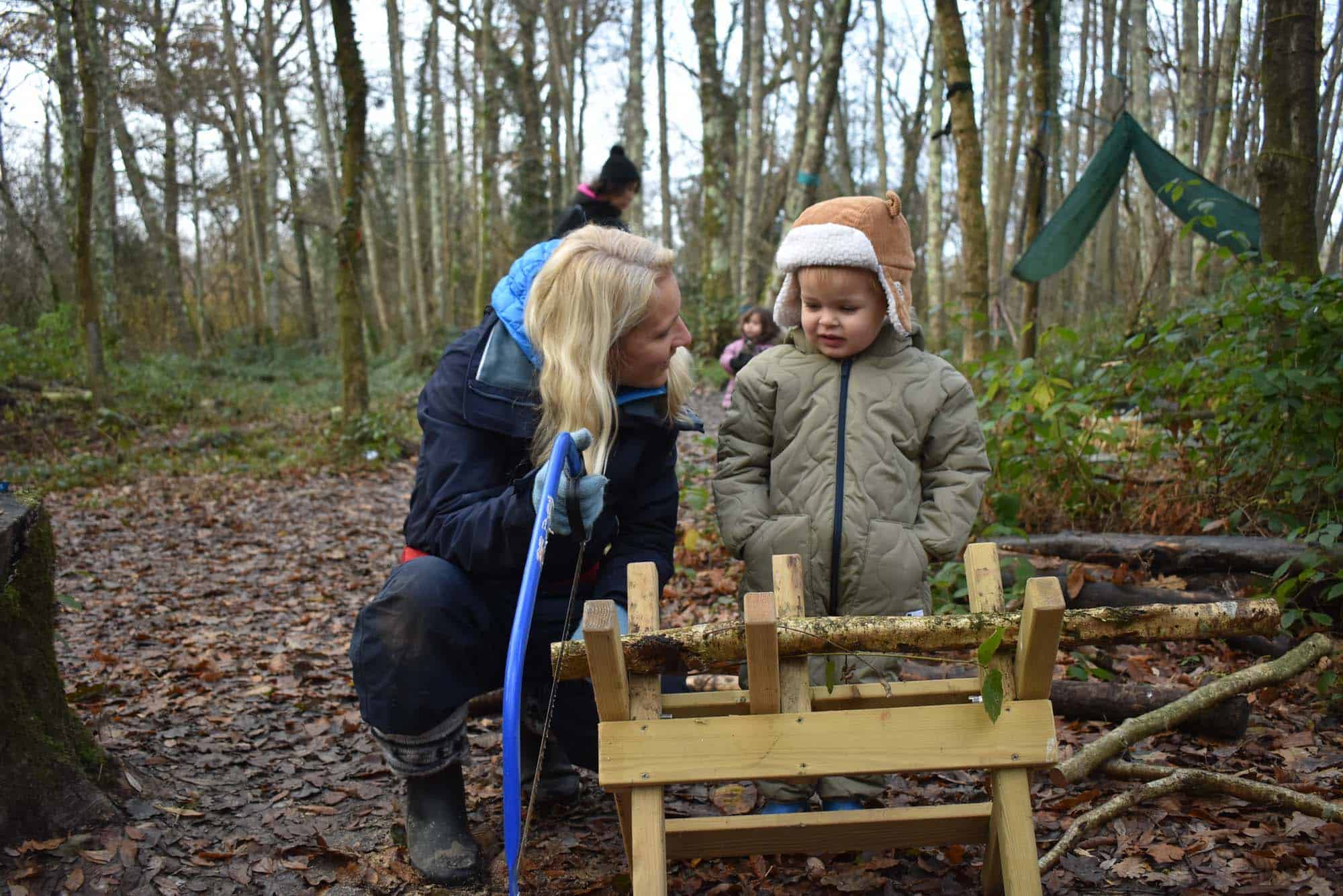 Teacher interacting with a toddler using some creative outdoor play equipment in a forest setting. Part of the toddler Group at Ardingly Nursery, in Mid Sussex.