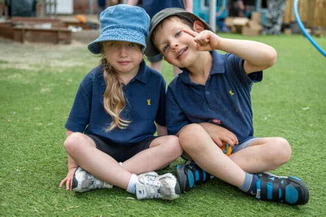 Two Nursery children sitting cross legged together on grass