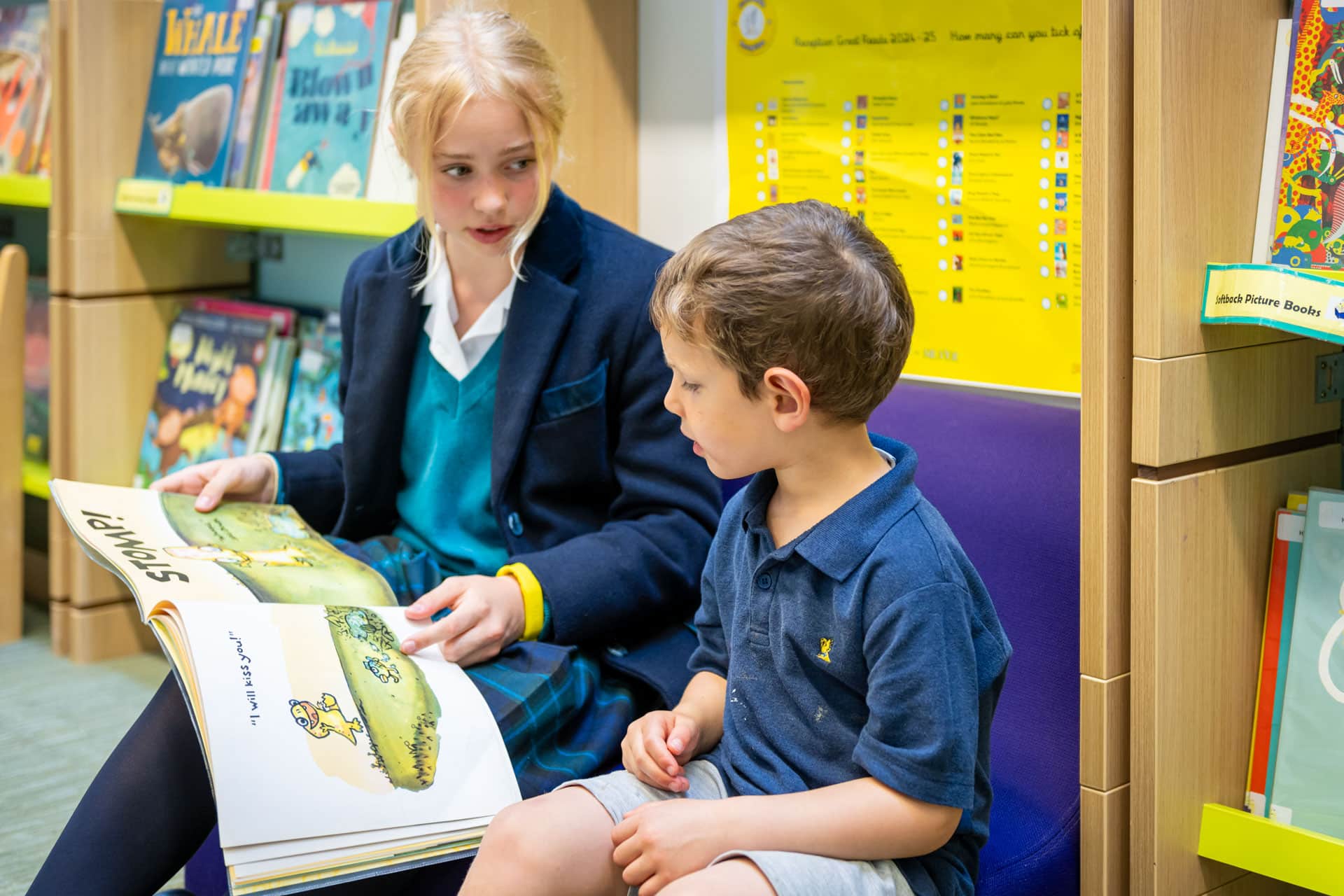 Older child reading a book to a Nursery child