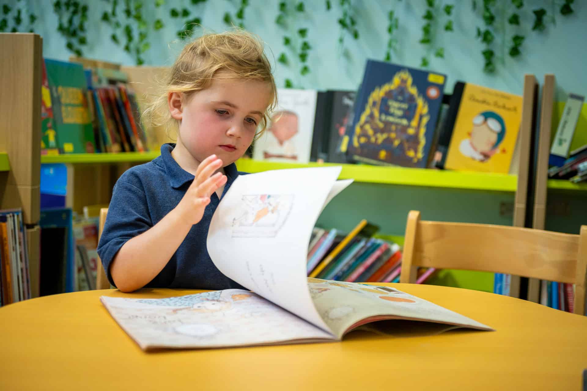 Nursery child reading a book in a library