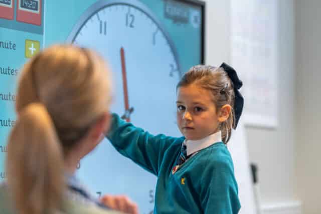 Girl showing the teacher the time in a classroom