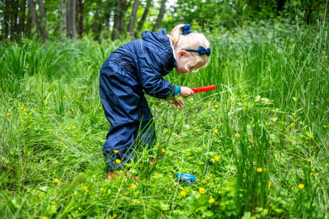 Prep children looking through a magnifying glass at forest school