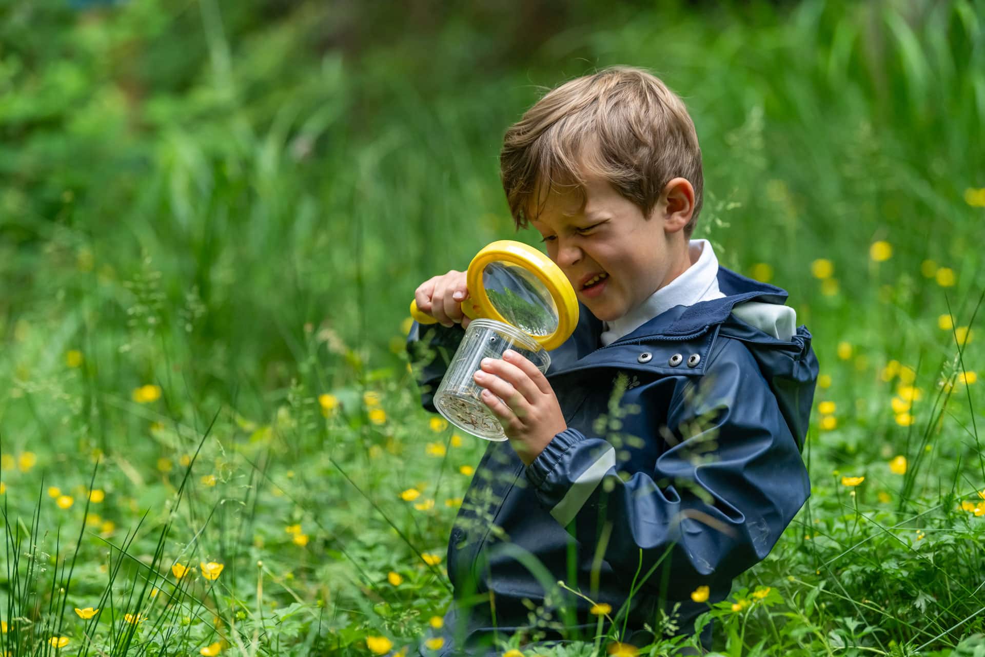 Prep children looking through a magnifying glass at forest school