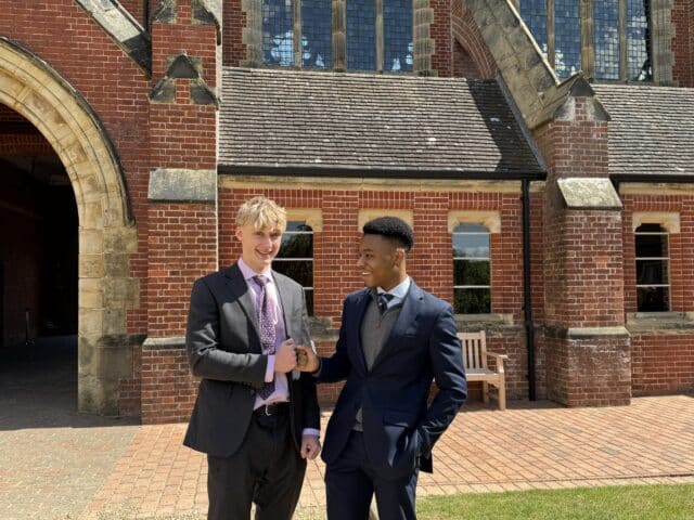 Three young women stand together outdoors, smiling and looking at papers they’re holding. They appear happy and excited, with arms round each other, in front of leafy trees on a grassy area.
