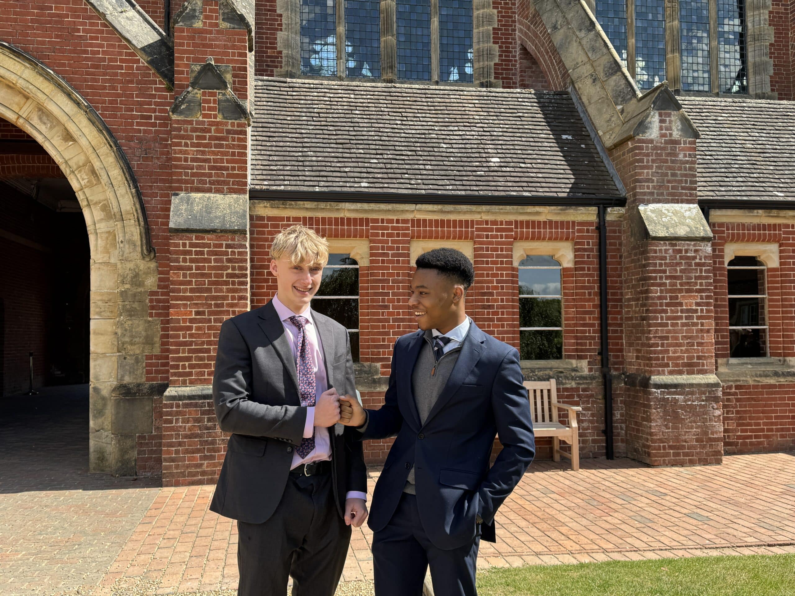 Three young women stand together outdoors, smiling and looking at papers they’re holding. They appear happy and excited, with arms round each other, in front of leafy trees on a grassy area.