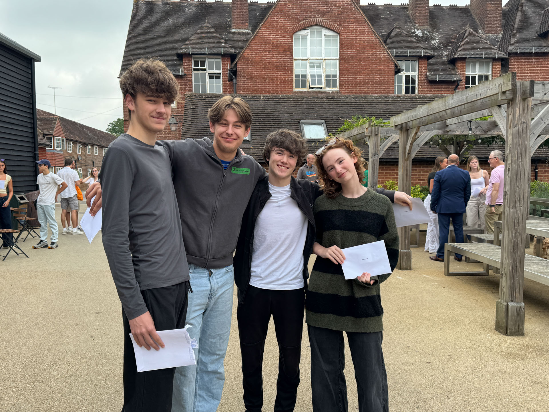 Four smiling teenagers stand arm-in-arm outdoors, holding A level results