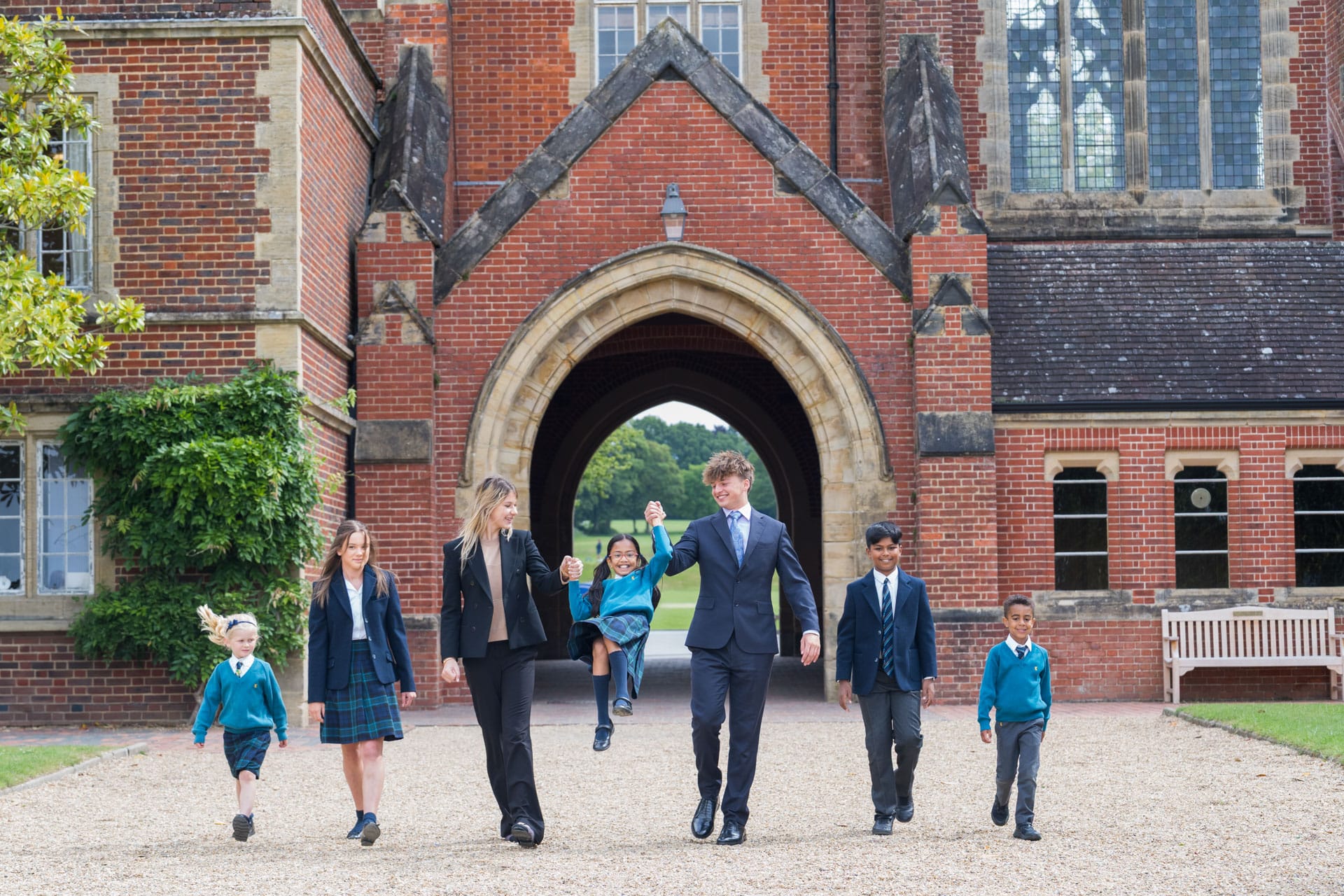 All aged children walking through the Archway with the oldest ones swinging a little girl from the Prep.