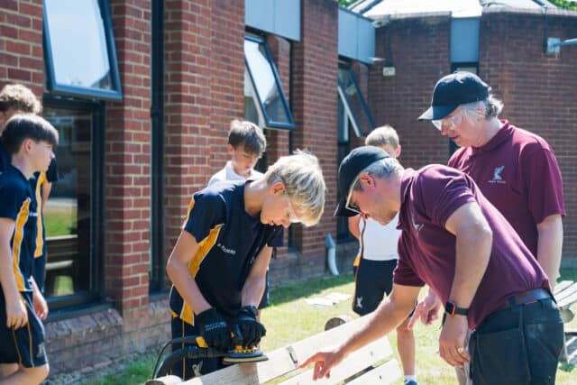 The maintenance department demonstrate how to sand a plank of wook during Life Skills Week, promoting practical learning and hands-on experience.