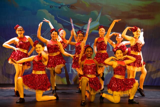 Dancers in air steward costumes perform a glamorous contemporary routine in Lost in Motion 2025.