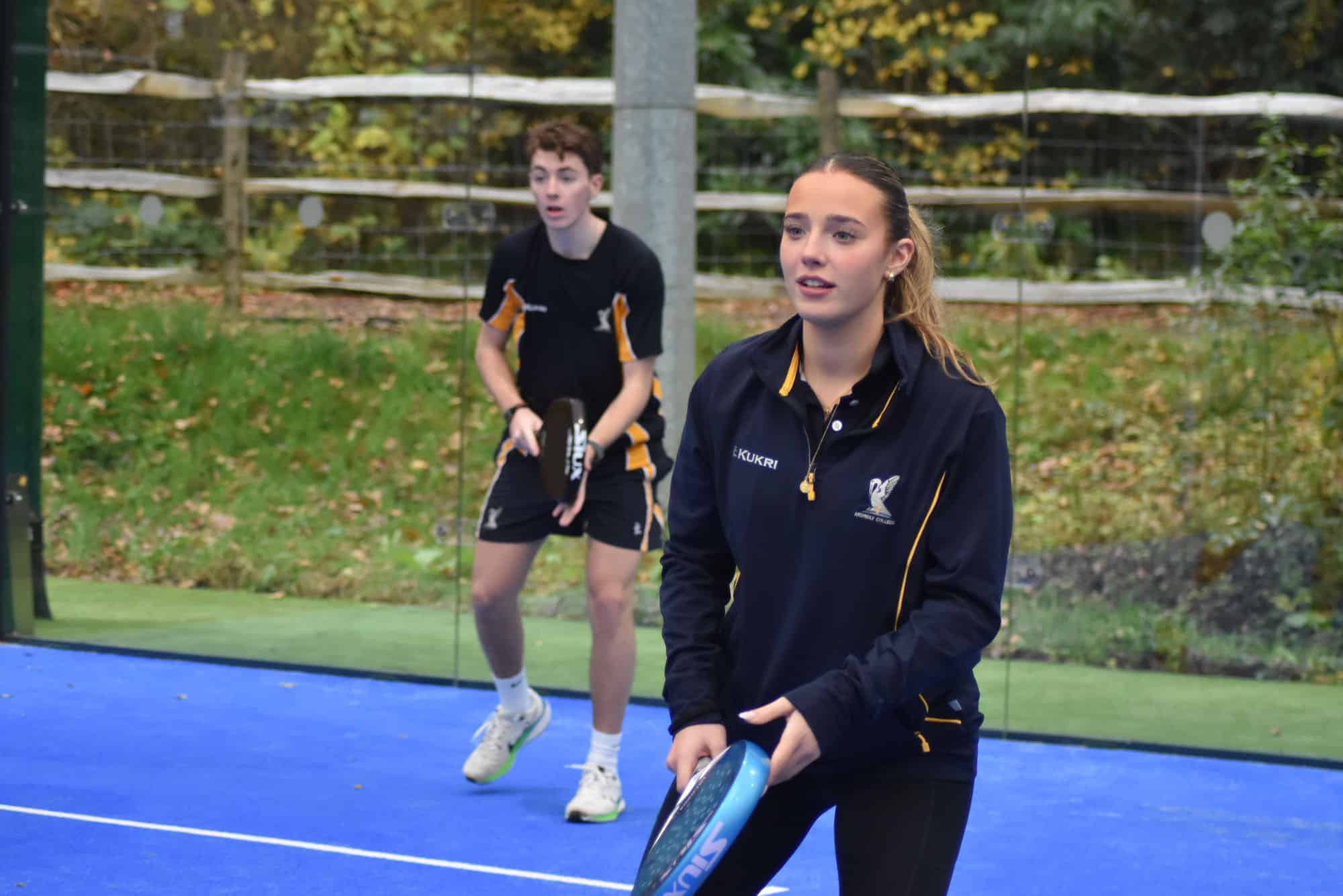 Two padel players on a blue court, one in the foreground holding a racquet and the other in the background holding a racquet.