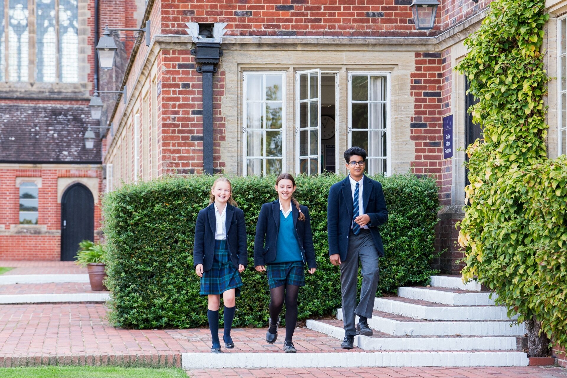 Three Ardingly Senior School students walking out of the Senior School reception building dressed in school uniform
